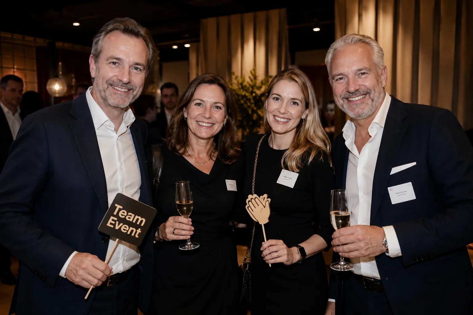 Vier festlich gekleidete Personen bei einem Firmenevent mit Champagner und Fotobox-Requisiten.